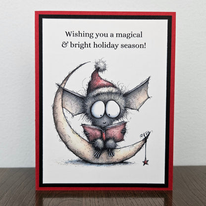Handmade Christmas bat card with festive bat reading on a crescent moon and magical bright holiday sentiment