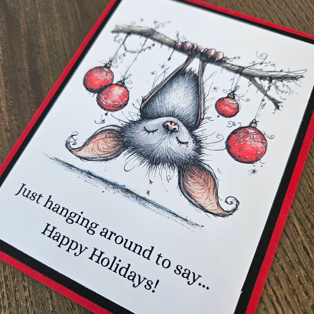  Angled close-up of upside-down bat illustration, red ornaments, and Happy Holidays wording.