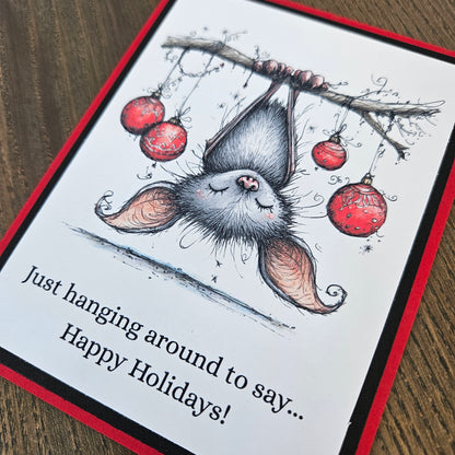  Angled close-up of upside-down bat illustration, red ornaments, and Happy Holidays wording.