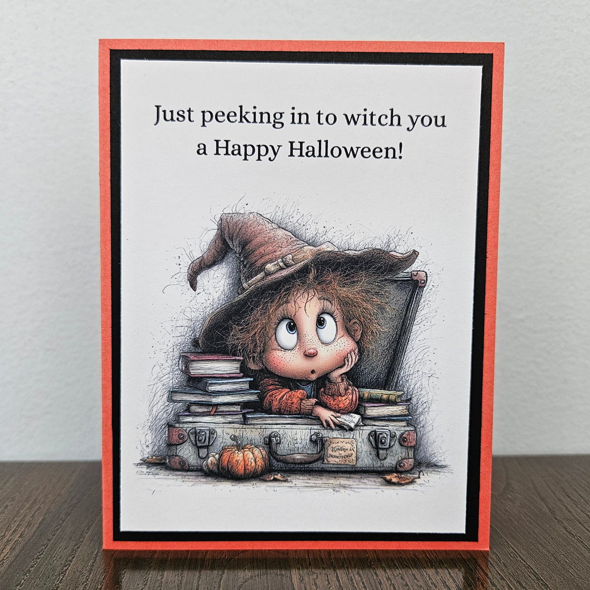 Handmade funny Halloween card with young witch peeking over spellbooks and a vintage trunk