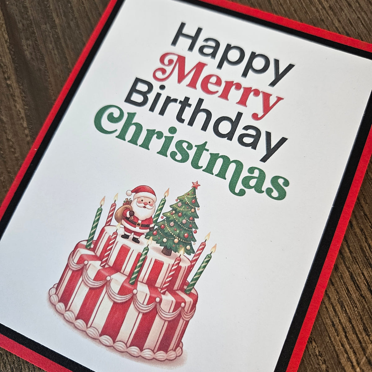 Angled close-up of the Christmas birthday card showing the text “Happy Merry Birthday Christmas,” Santa, a decorated tree, and a festive cake.
