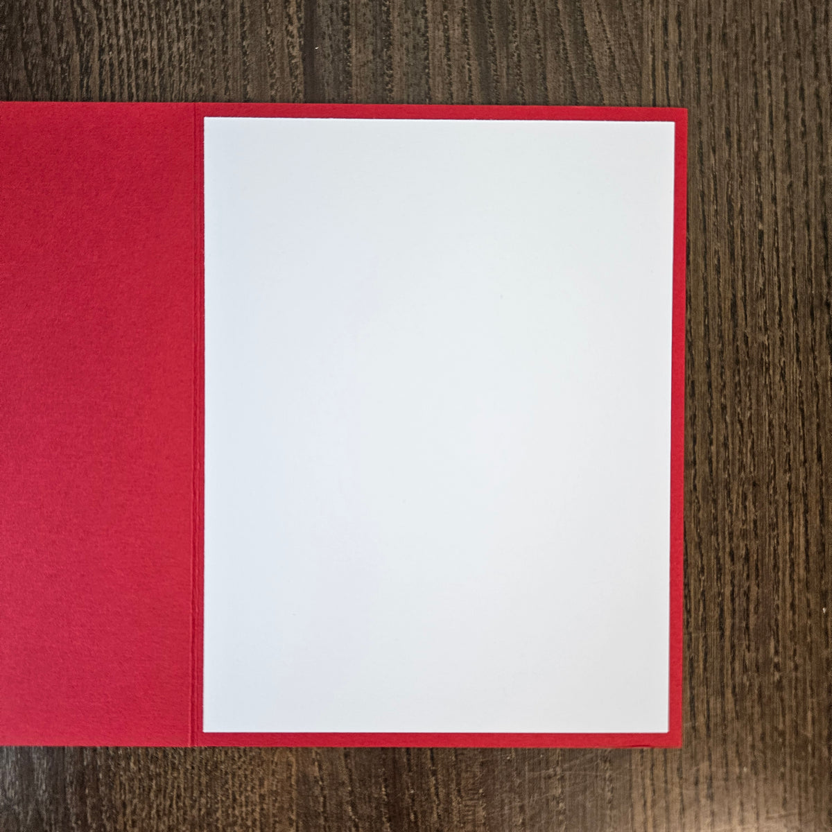 A blank white card centered inside a red envelope or folder, photographed from above on a dark wood-grain surface.