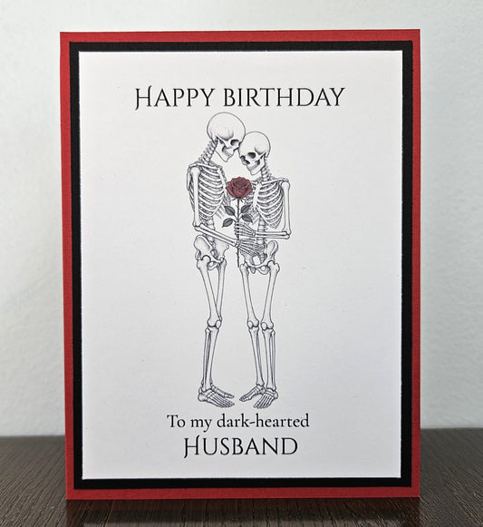 Handmade red and black birthday card with an embracing skeleton couple, red rose, and Happy Birthday to my dark-hearted husband wording.
