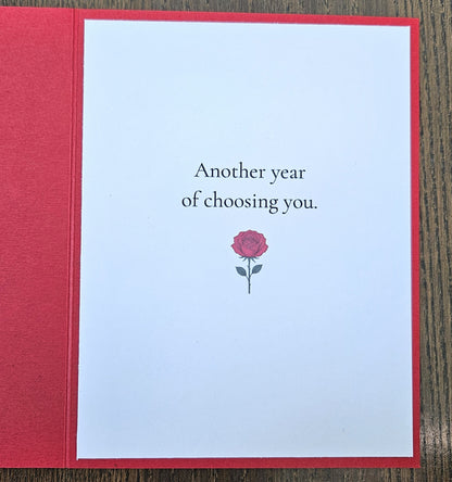 Inside of red husband birthday card reading Another year of choosing you, with a small red rose illustration.