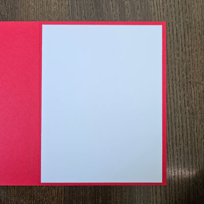 A blank white rectangular card or paper sheet with a bright red border, placed on a dark brown wood-grain surface.