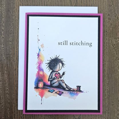Still stitching gothic encouragement card laid on a wooden surface with its included white envelope.