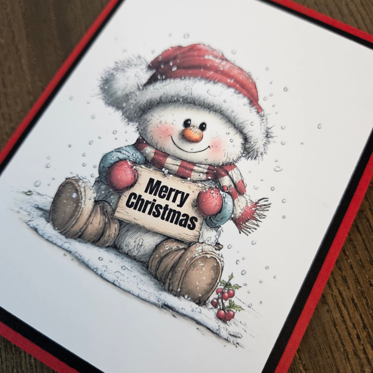 Angled close-up of the snowman, Merry Christmas sign, snowy illustration, and red and black cardstock borders.