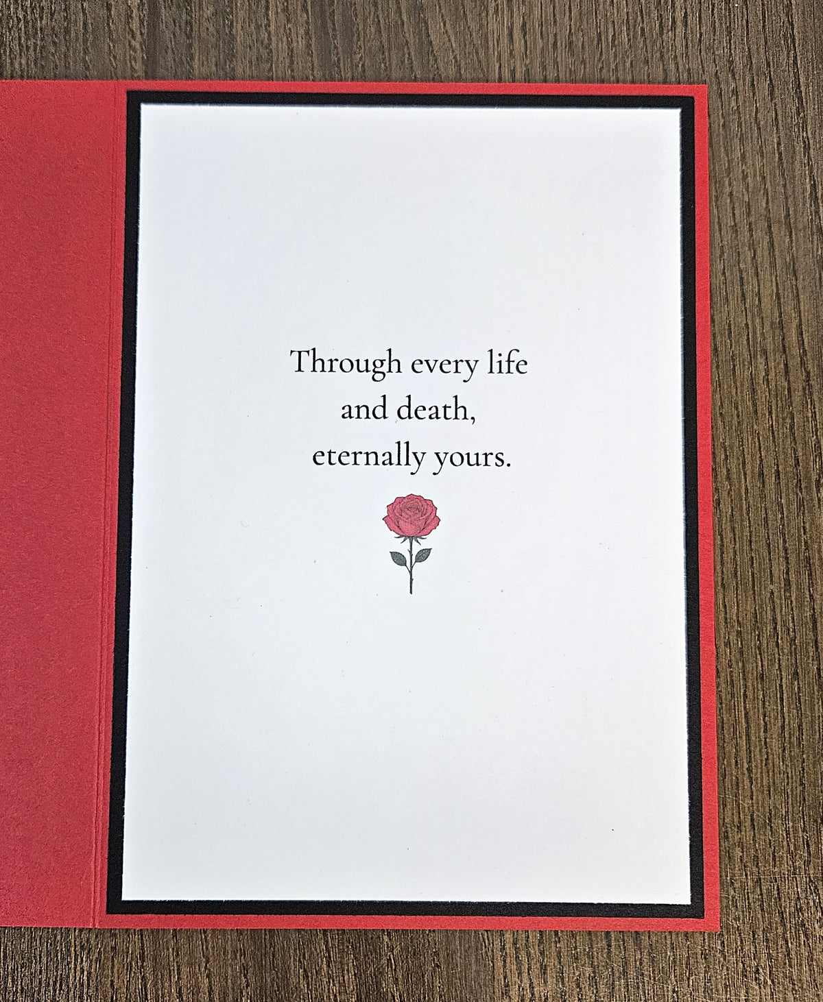 Printed inside message reading Through every life and death, eternally yours, with a rose illustration on a black-matted white panel inside the red card.