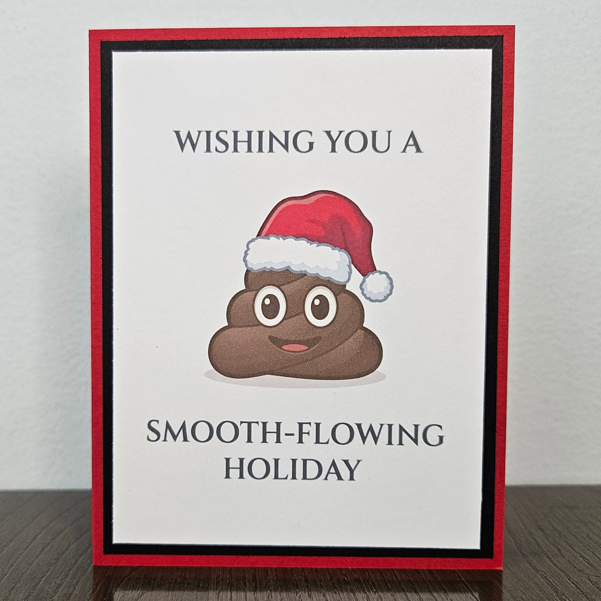 Handmade red and black Christmas card with a smiling poop emoji in a Santa hat and Wishing you a smooth-flowing holiday wording.
