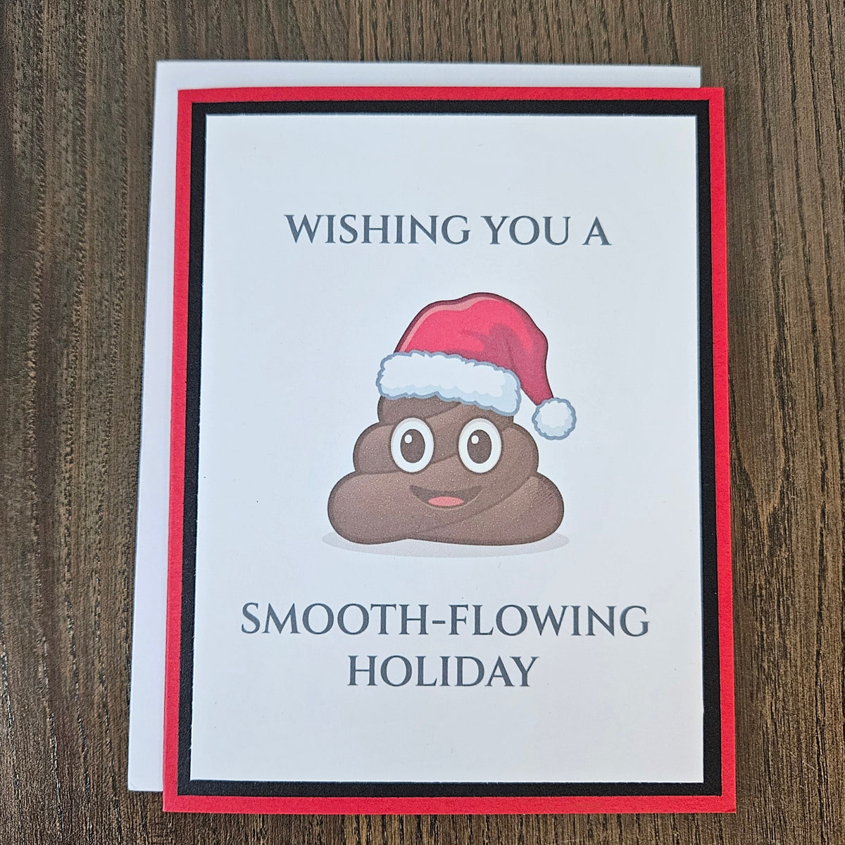 Red and black smooth-flowing holiday poop emoji Christmas card shown with its included white envelope.