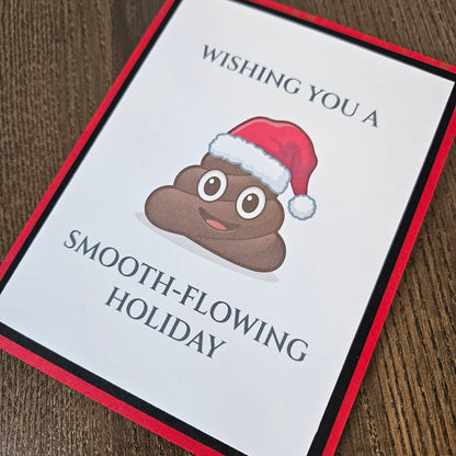 Angled close-up of the Santa-hat poop emoji, smooth-flowing holiday greeting, and red and black cardstock layers.