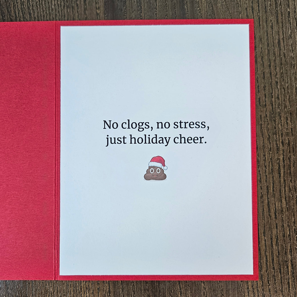 Inside of red Christmas card reading No clogs, no stress, just holiday cheer, with a small poop emoji in a Santa hat.