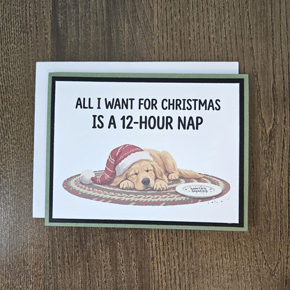 Green and black sleeping-dog Christmas card shown with its included white envelope on a wooden surface.