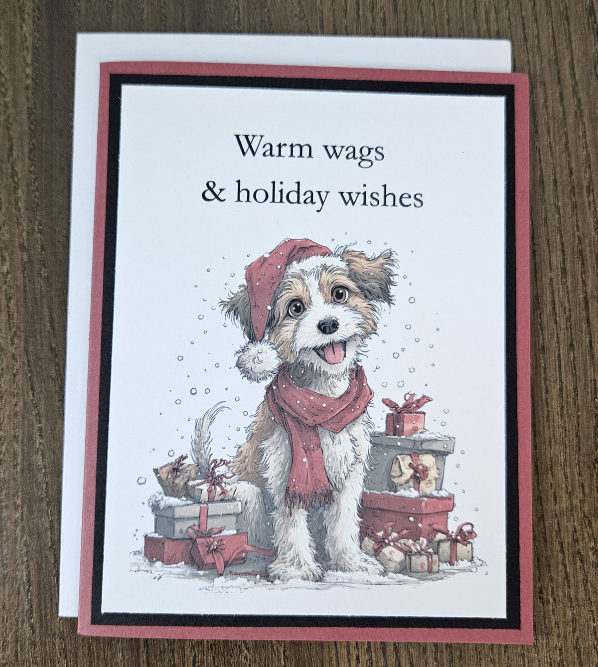 Warm wags and holiday wishes dog Christmas card laid on a wooden surface with its included white envelope.