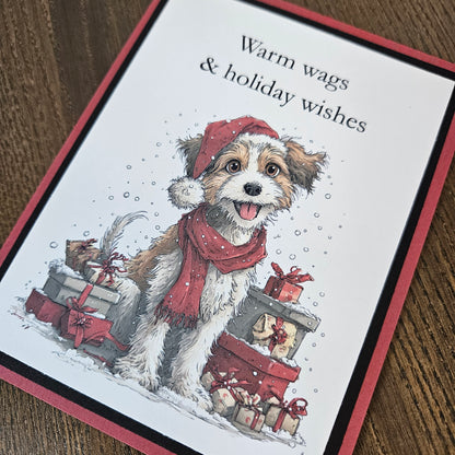 Angled close-up of the festive dog, wrapped gifts, snowy details, and muted red and black cardstock borders on the Warm wags Christmas card.