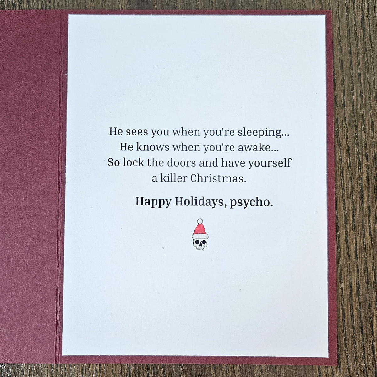 Inside of burgundy Grim Reaper Christmas card with a sleeping and awake rhyme, a killer Christmas punchline, Happy Holidays psycho, and a Santa-hat skull.