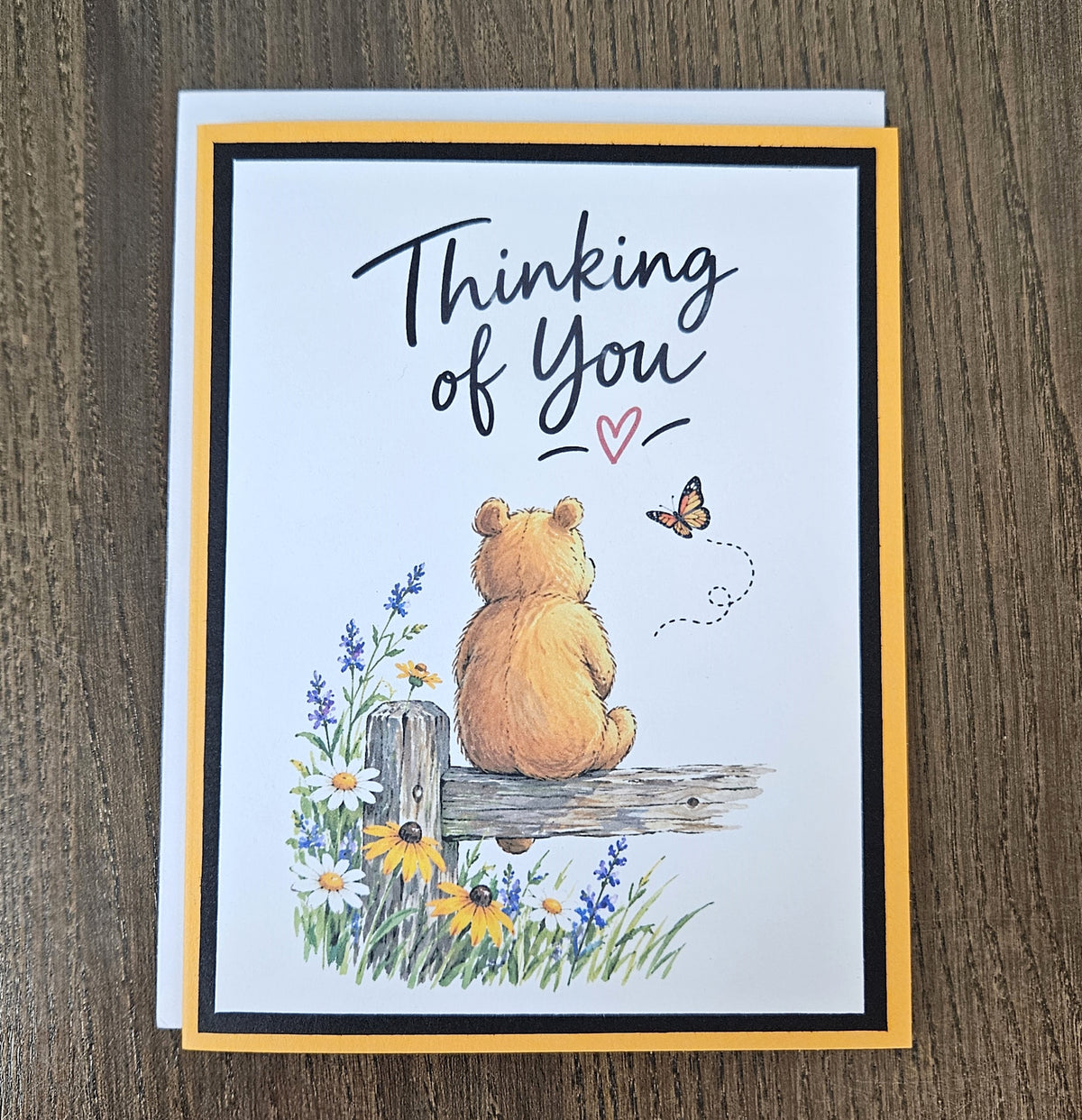 Thinking of You bear and butterfly greeting card lying flat with a white envelope behind it.