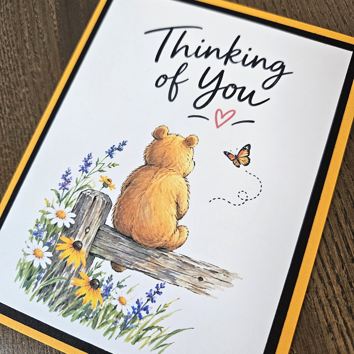Angled close-up of the bear, butterfly and wildflower illustration on a layered Thinking of You greeting card.