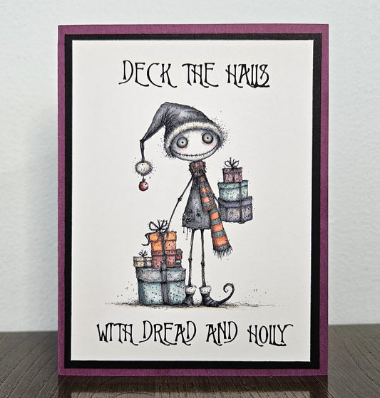 Angled close-up of the spooky festive character, striped scarf and wrapped presents on the layered purple and black Christmas card.