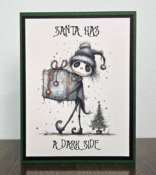 Handmade gothic Christmas card reading Santa Has a Dark Side, with a skeleton in a Santa hat carrying a gift beside a tiny tree, framed in black and green.