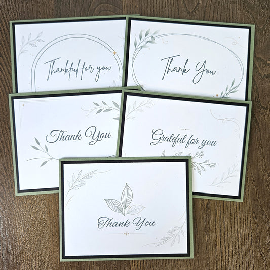 Set of five handmade sage green botanical thank-you cards with black layers and assorted gratitude sentiments, arranged on wood.