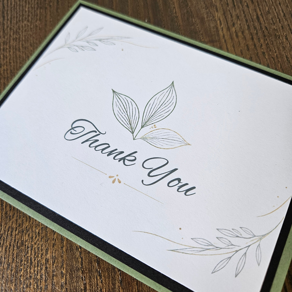 Angled close-up of Thank You card with a three-leaf illustration, delicate corner foliage and sage green base.