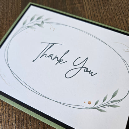 Thank You script inside a delicate oval frame with green leaves and small gold-colored printed accents.