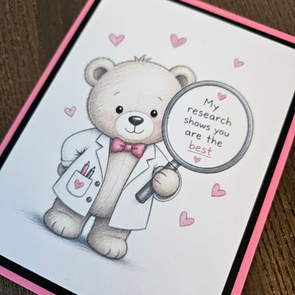 Angled close-up of the teddy bear in a white lab coat and pink bow tie, holding a magnifying glass surrounded by pink hearts.