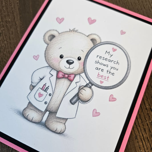 Angled close-up of the teddy bear in a white lab coat and pink bow tie, holding a magnifying glass surrounded by pink hearts.