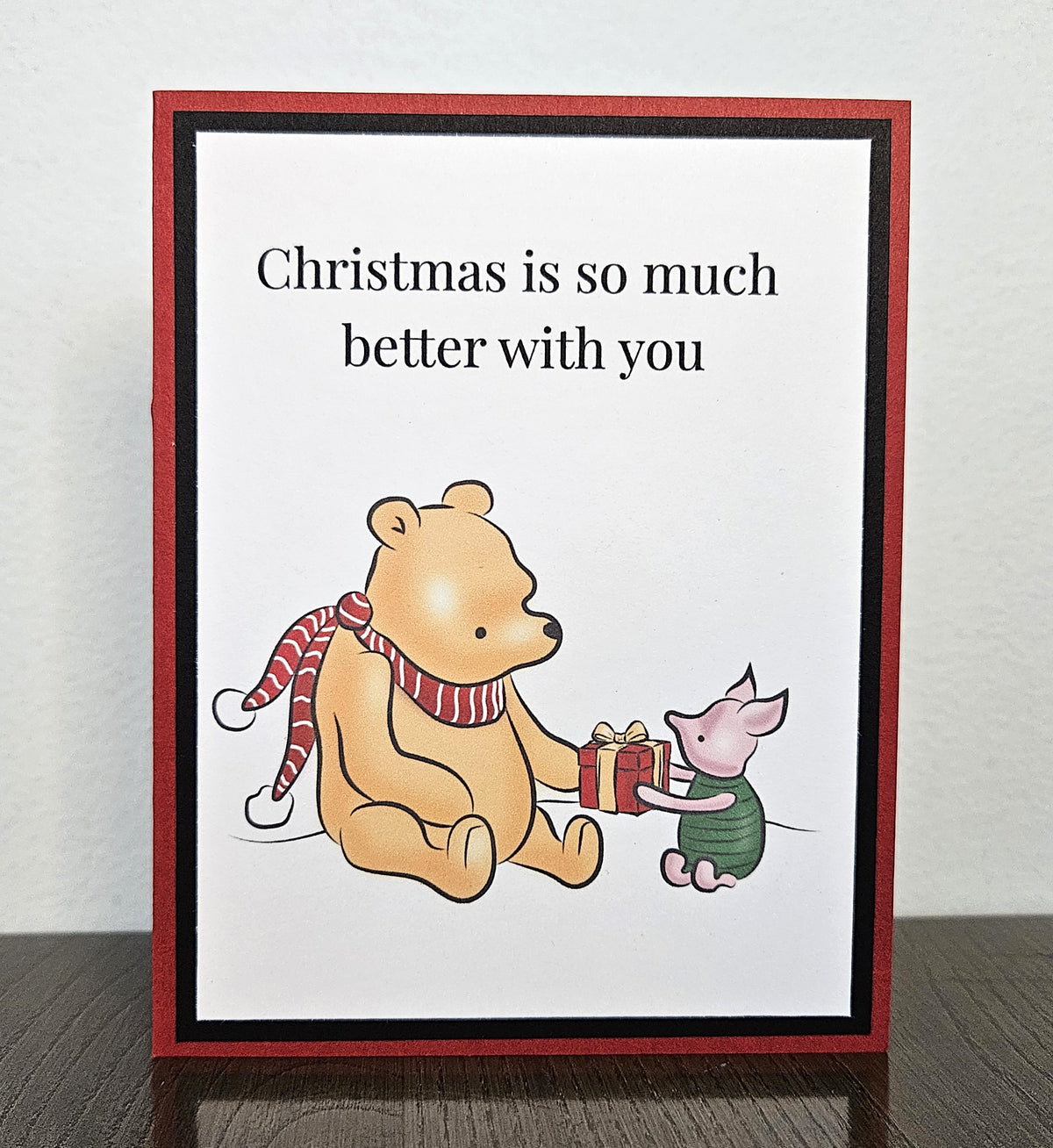 Standing front of a handmade Winnie the Pooh and Piglet Christmas card sharing a present, with Christmas is so much better with you above the illustration.