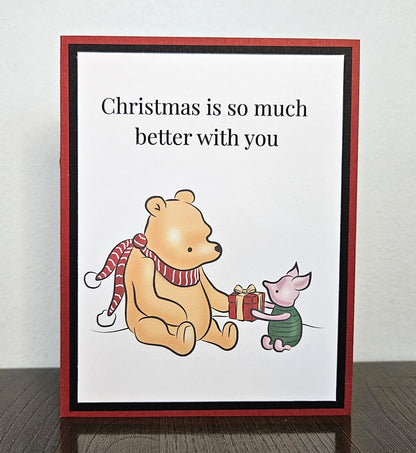 Standing front of a handmade Winnie the Pooh and Piglet Christmas card sharing a present, with Christmas is so much better with you above the illustration.