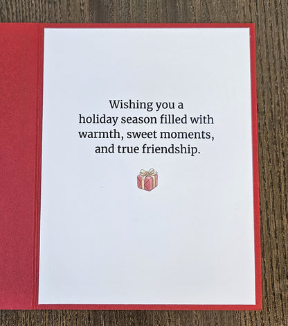 Printed inside of the red Christmas card reading Wishing you a holiday season filled with warmth, sweet moments, and true friendship, with a small present below.