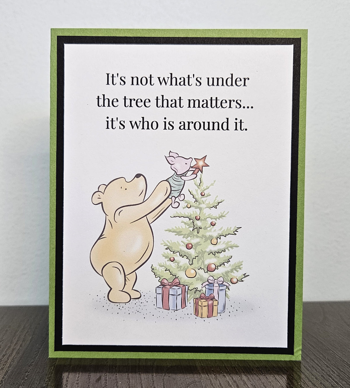 Standing front of a handmade Pooh Christmas card showing Pooh lifting Piglet to place a star on a Christmas tree, framed in black on a green card base.