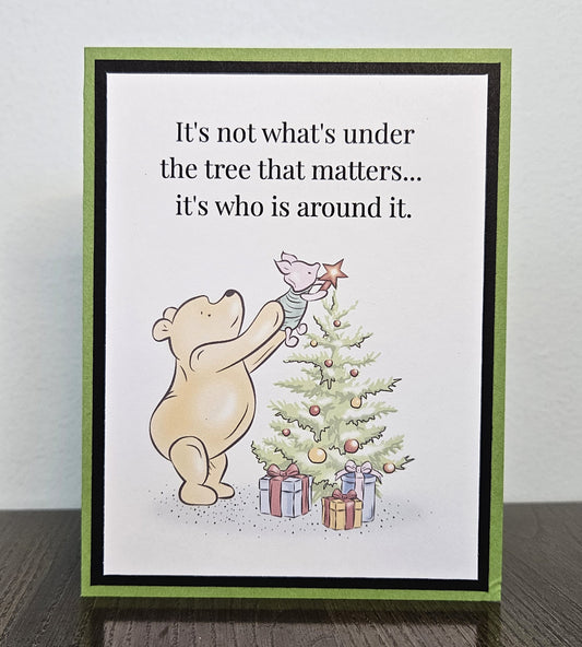 Standing front of a handmade Pooh Christmas card showing Pooh lifting Piglet to place a star on a Christmas tree, framed in black on a green card base.