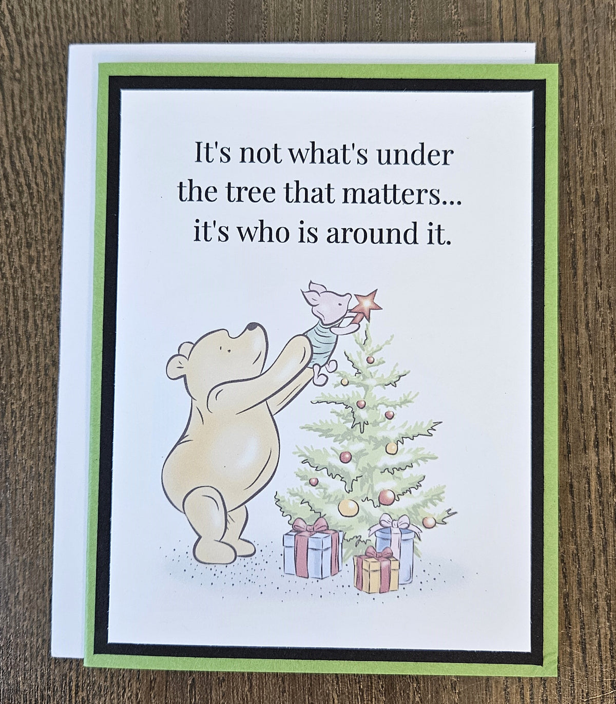 Green and black handmade Pooh and Piglet Christmas tree card with a white envelope on a wooden surface.