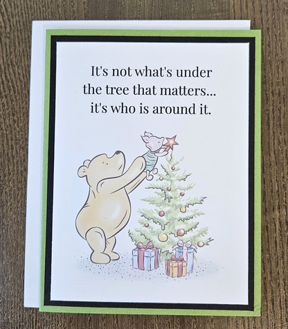 Green and black handmade Pooh and Piglet Christmas tree card with a white envelope on a wooden surface.
