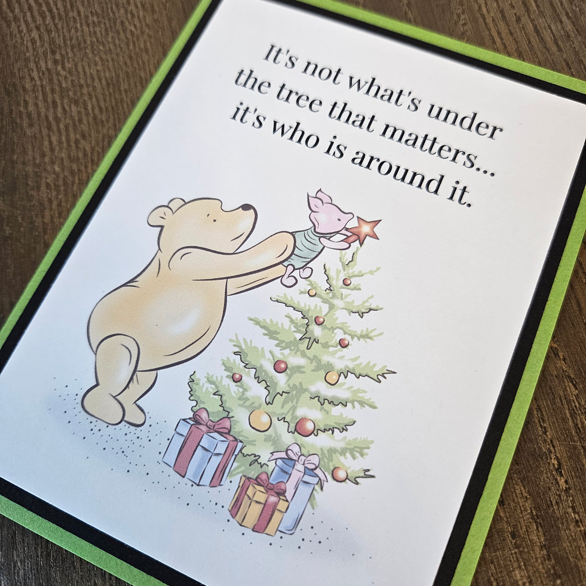 Angled close-up of Pooh and Piglet decorating a Christmas tree beneath the words It's not what's under the tree that matters... it's who is around it.