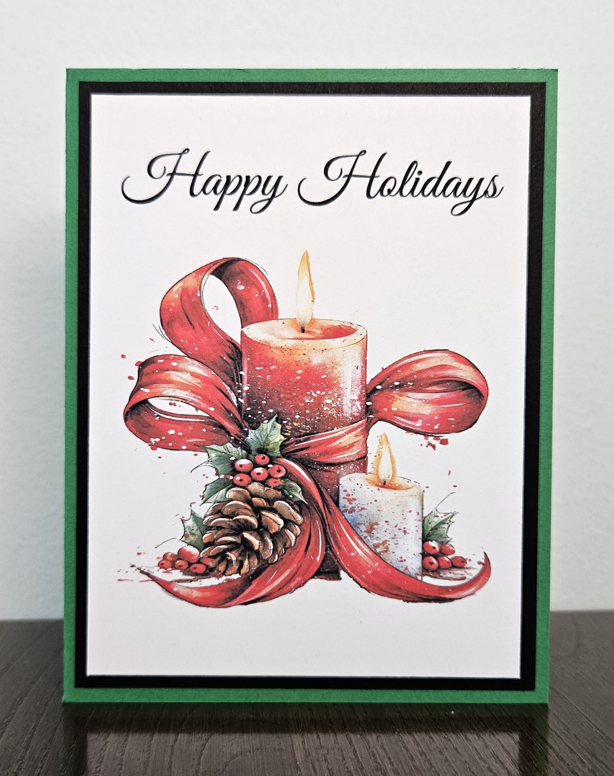Handmade Happy Holidays card with candles, red ribbon, holly berries and a pinecone, framed in black and green cardstock.