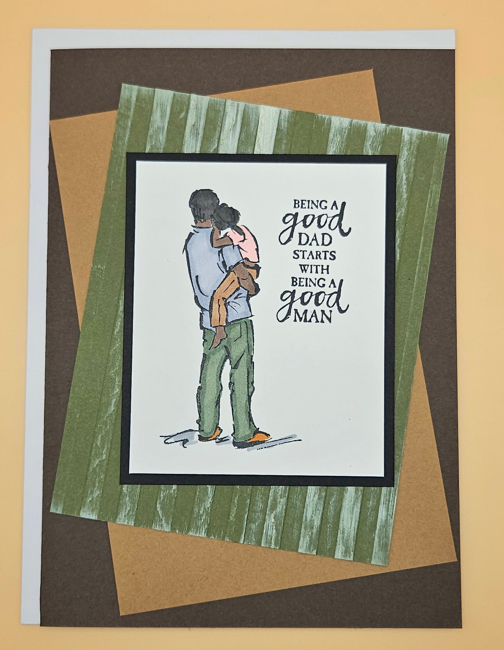Card with illustration of a black father holding a child and text 'Being a good dad starts with being a good man' on a striped background.
