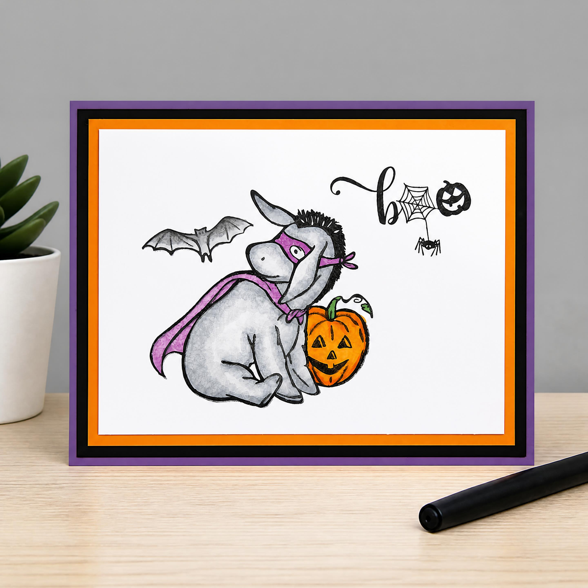 Handmade Winnie the Pooh Halloween card featuring hand-colored Eeyore in a purple superhero costume beside a jack-o’-lantern.