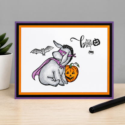 Handmade Winnie the Pooh Halloween card featuring hand-colored Eeyore in a purple superhero costume beside a jack-o’-lantern.