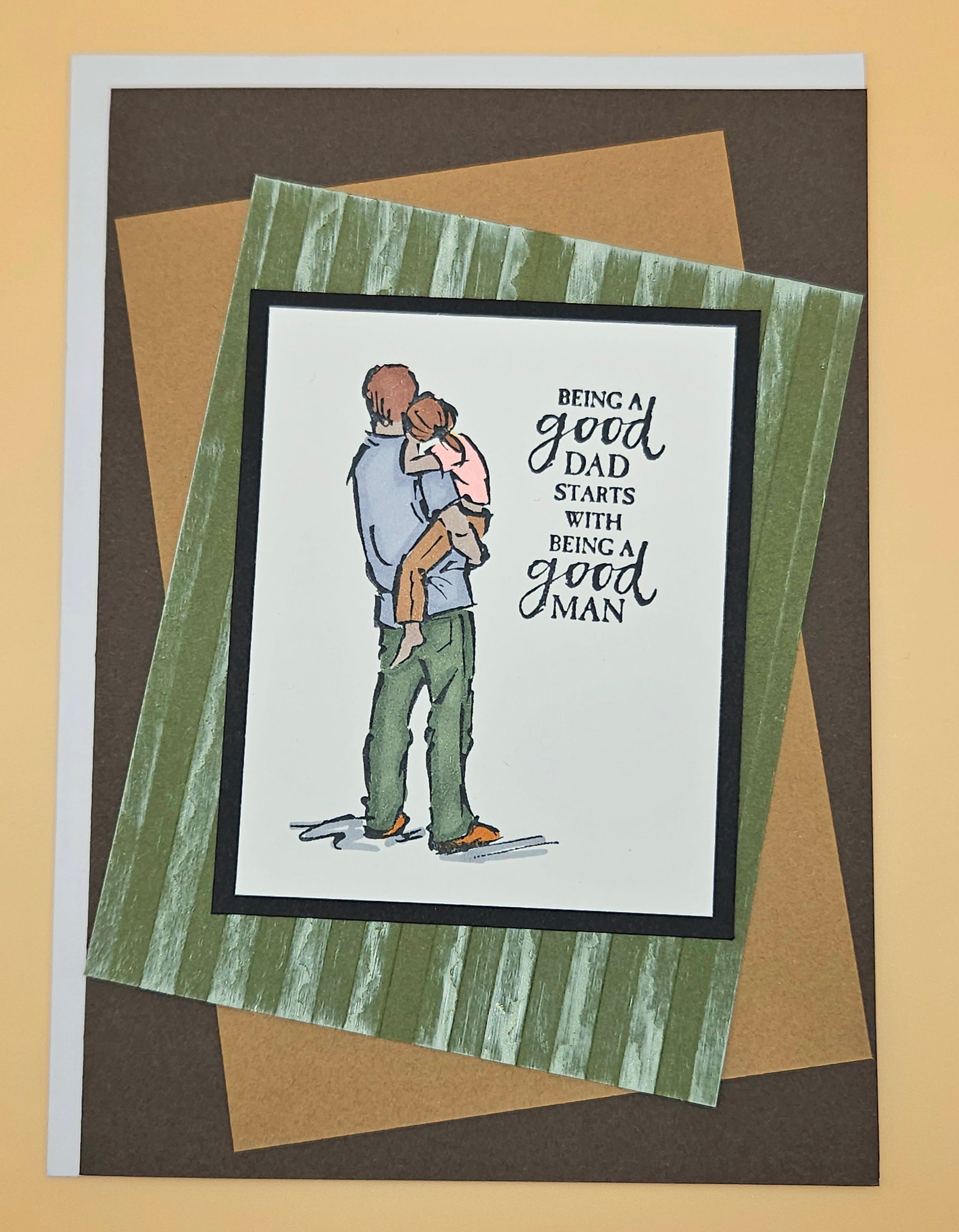 Card with illustration of a latino father holding a child and text 'Being a good dad starts with being a good man' on a striped background.