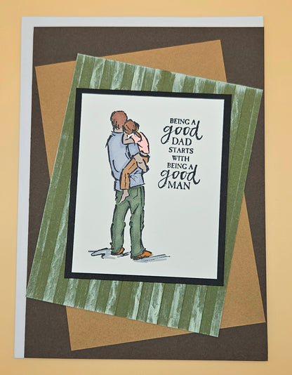 Card with illustration of a latino father holding a child and text 'Being a good dad starts with being a good man' on a striped background.